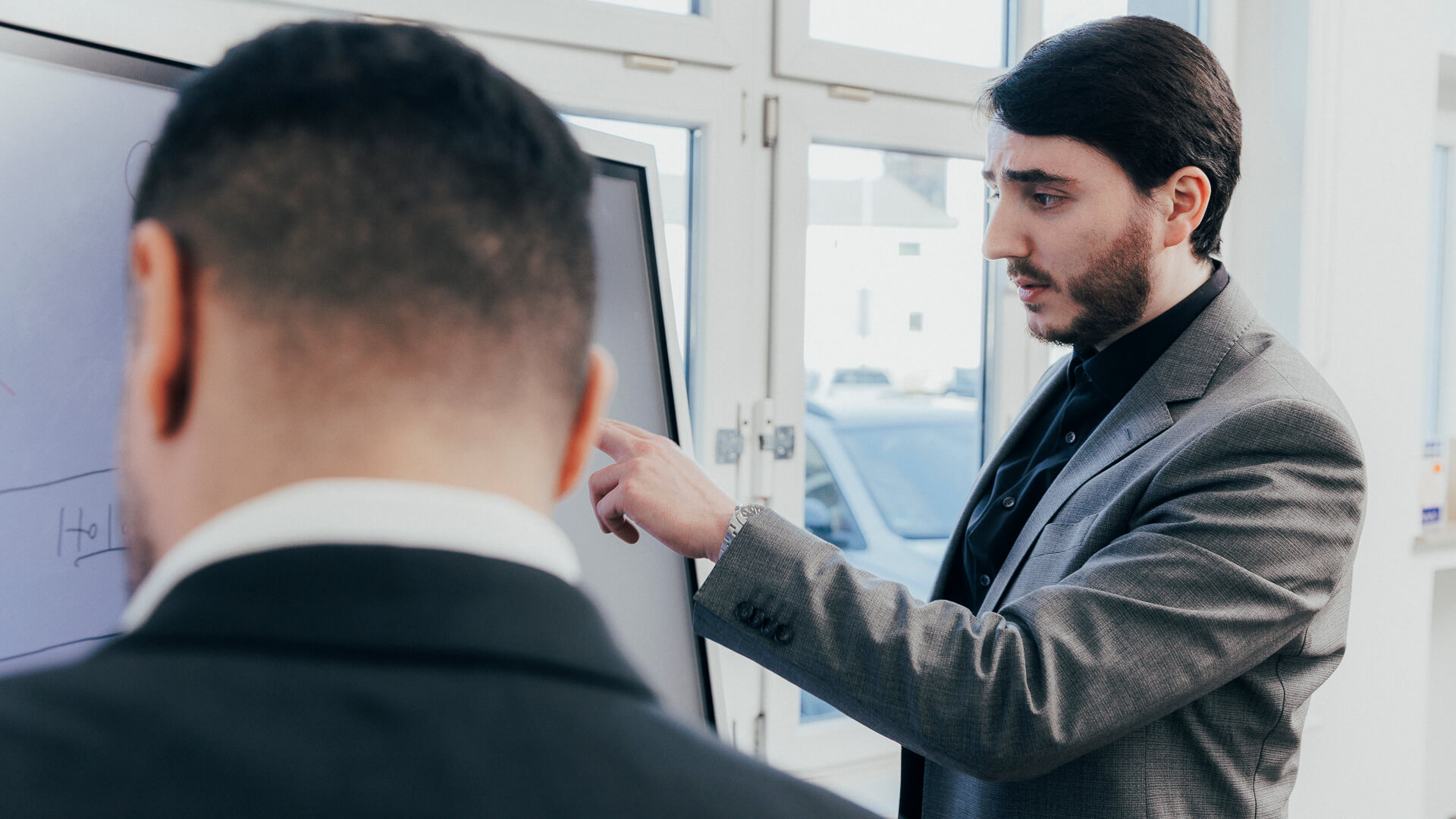Ein Steuerberater für Schenkungssteuer zeigt auf ein Whiteboard, während ein weiterer daneben steht